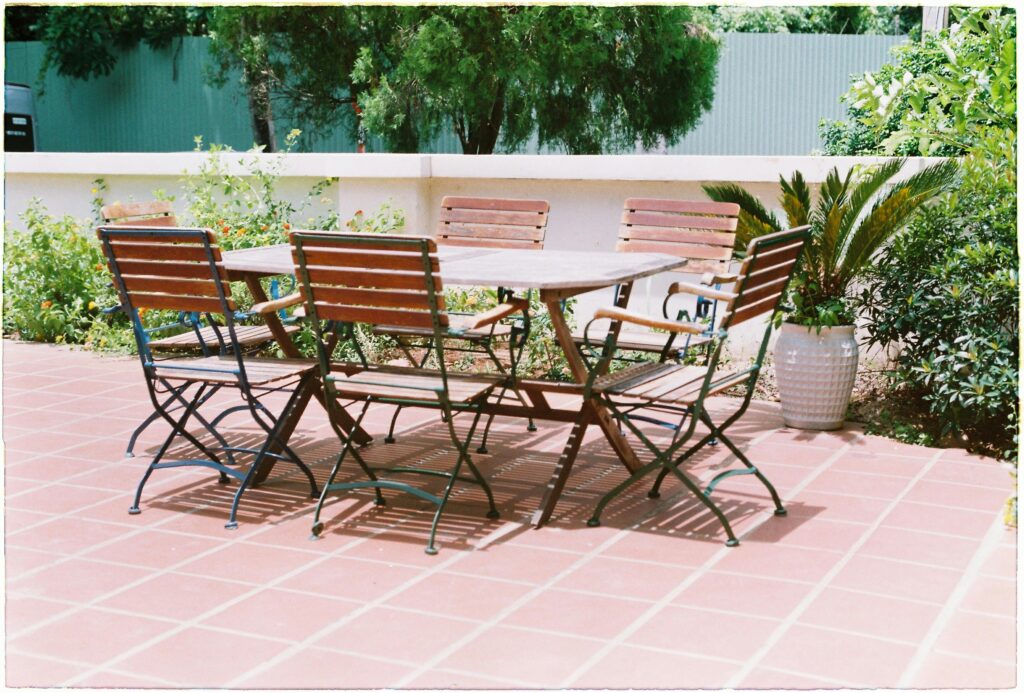 Salon de jardin en bois et métal installé sur une terrasse revêtue de carrelage en terre cuite rouge.